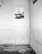 Ausstellungsinszenierung "Kristallnacht" im Jahr 1992. Schwarz-weiß Aufnahme mit einem Bild der ehemaligen Synagoge an einer kahlen Betonwand. Davor auf dem Boden liegen Scherben und ein gerahmtes Bild der Synagoge.