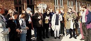 Gruppe von Siegener Lehrern mit dem ehemaligen Auschwitz-Häftling Artur Radvansky (Bildmitte) vor einer Backsteinbaracke auf dem Gelände des ehemaligen Konzentrationslagers Auschwitz. Farbige Aufnahme.